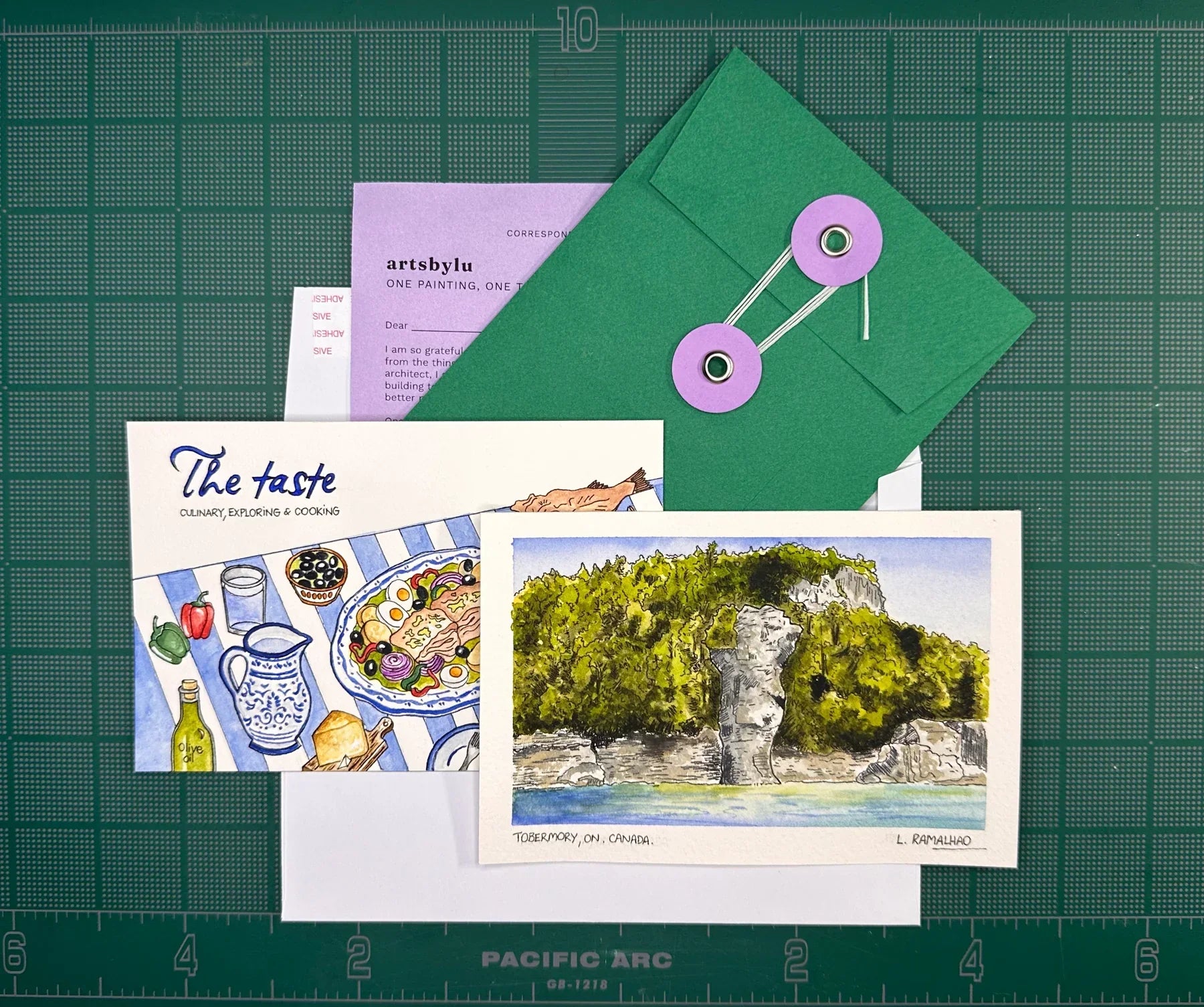 The October 2026 edition laid out: a watercolour print of Tobermory, the painted recipe card, a handwritten letter, and the handmade green envelope tied shut with string
